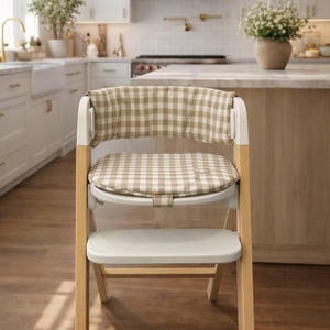May include: A wooden high chair with a beige and white checkered seat and backrest cushion. The chair has a white footrest and a light wood frame. The chair is designed for a baby or toddler.