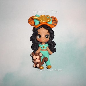 May include: A handcrafted polymer clay figurine of a cartoon character, wearing a teal outfit and a headband with a golden lamp. The figurine is holding a brown monkey. The text "Cloud Nine Clays" is visible.