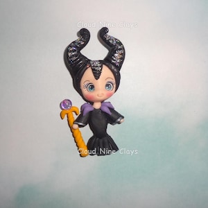 May include: A small clay figurine of a character with large blue eyes, wearing a black dress with a purple collar and large black horns accented with silver glitter. The figure holds a yellow staff topped with a purple orb. Text reads Cloud Nine Clays.