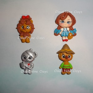May include: Four Wizard of Oz characters made of polymer clay. The characters are Dorothy, the Cowardly Lion, the Tin Man, and the Scarecrow. Each character is about 2 inches tall and has a whimsical, cartoonish style.