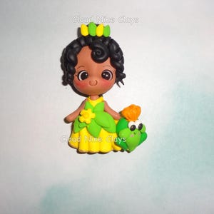 May include: A clay figurine of a character with dark curly hair, a yellow dress with green leaf accents, and a yellow flower. The character has a small green frog companion with an orange flower on its head. Text reads Cloud Nine Clays.