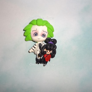 May include: A handmade clay figurine of a character with green hair and a black and white striped suit, holding a smaller figurine with black hair and a red outfit. The figurines are on a light blue background. The text "Cloud Nine Clays" is visible.