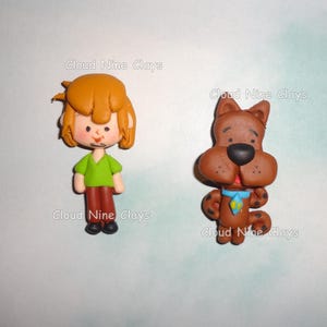 May include: Two clay figurines: one of a cartoon character with orange hair, a green shirt, and brown pants, and another of a brown cartoon dog with a blue collar. The text "Cloud Nine Clays" is visible.
