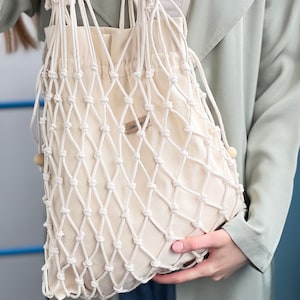 Peut inclure: Un sac fourre-tout en filet de coton blanc avec une fermeture à cordon. Le sac porte une étiquette indiquant "Cotton & Co."