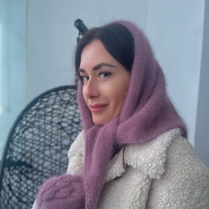 Puede incluir: Una mujer con una bufanda de punto morada y una chaqueta de piel sintética blanca. La bufanda está atada alrededor de su cuello y la chaqueta está abrochada.