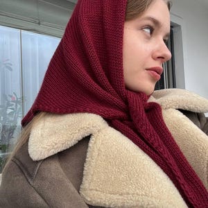 Może przedstawiać: Kobieta w bordowym dzianym szaliku i brązowej kurtce z imitacji futra z kremową podszewką.
