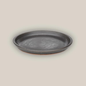May include: A dark gray, ceramic plate with a slightly textured surface. The plate has a low, rounded rim and a reddish-brown base. The plate is circular and appears to be handmade.
