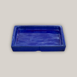 May include: A rectangular blue ceramic tray with a slightly raised rim. The tray is glazed and has a smooth, glossy finish.