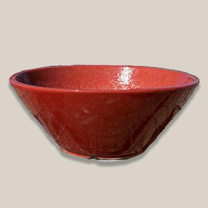 May include: A glossy, red ceramic bowl with a textured, geometric pattern on the exterior. The bowl has a wide, oval shape and a slightly raised rim. The interior is a solid, vibrant red. This decorative bowl is suitable for serving or display.