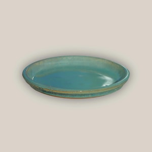 May include: A handmade, turquoise-glazed ceramic plate. The plate has a shallow, oval shape with a slightly raised rim. The glaze has a glossy finish, and the rim features a textured, earthy band of color.