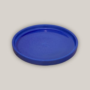 May include: A round, blue ceramic tray with a slightly raised rim. The tray has a smooth, glossy finish.