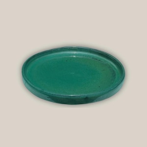 May include: A round, emerald green ceramic plate with a slightly raised edge. The plate has a smooth, glossy finish and a simple, minimalist design. The plate is suitable for serving food.