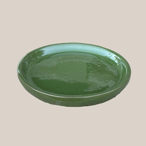 May include: A round, green ceramic plate with a glossy finish. The plate has a slightly raised rim and a smooth, flat surface. The color is a deep, rich green, and the plate appears to be handmade.