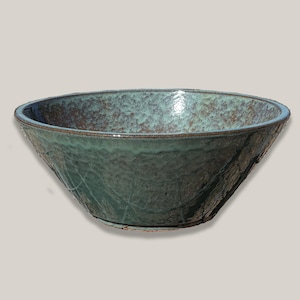 May include: A wide, circular ceramic bowl featuring a mottled teal and dark brown glaze. The exterior surface has a textured, hammered appearance, while the interior displays a smooth, glossy finish with subtle variations in color and tone.