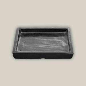 May include: A rectangular, black tray with a slightly textured surface. The tray has raised edges and a minimalist design. The dark color and simple shape suggest a modern aesthetic, suitable for various uses.