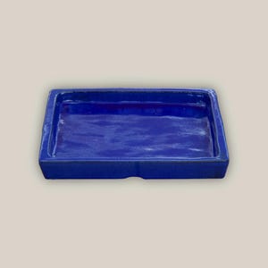 May include: A rectangular, cobalt blue ceramic tray with a glossy finish. The tray has slightly raised edges and a smooth interior surface. The overall design is simple and modern, suitable for various uses.