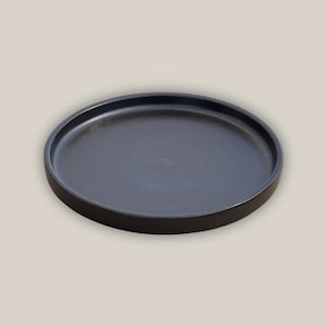 May include: A round, black serving tray with a raised edge. The tray has a matte finish and a simple, minimalist design. The tray is suitable for serving food or displaying decorative items.