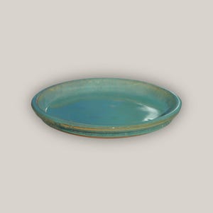 May include: A teal ceramic saucer with a slightly raised rim. The saucer has a subtle, textured finish.