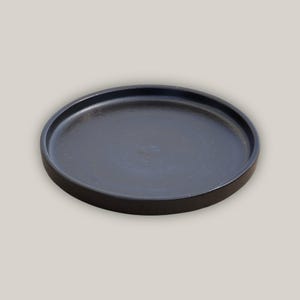 May include: A black ceramic tray with a smooth, slightly textured surface. The tray is round and has a raised rim.