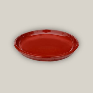 May include: A red, round, ceramic plate with a slightly raised rim.