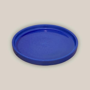 May include: A round, cobalt blue tray with a raised edge. The tray has a smooth, glossy finish and is designed for serving or display. The tray is approximately 10 inches in diameter.