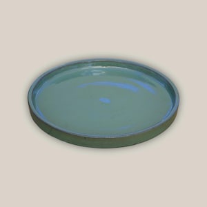 May include: A round, shallow, ceramic plate with a slightly raised rim. The plate is a muted teal color with a glossy finish. The rim is a darker shade of teal. The plate is suitable for serving food.