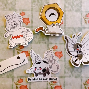 May include: Five colourful cartoon character stickers with white backgrounds. The stickers feature a white and red chameleon, a white and grey butterfly, a grey and white creature with a red eye, a white and grey creature with a red eye and a yellow and white creature with a red eye. The stickers have the text "Be kind to our planet." printed below them.