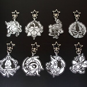 May include: Eight black and white constellation-themed keychains with silver star-shaped charms and silver rings. Each keychain features a different constellation design with letters and symbols.