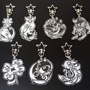 May include: Set of eight silver keychains with black and white constellation designs. Each keychain features a different constellation with a star-shaped charm at the top.