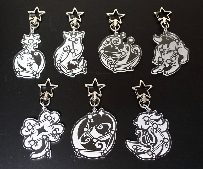 May include: Set of eight silver keychains with black and white constellation designs. Each keychain features a different constellation with a star-shaped charm at the top.