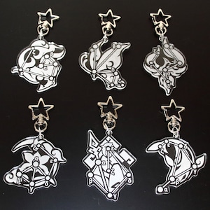 May include: Six black and white keychains with different designs. Each keychain features a star-shaped charm and a unique design with letters and lines. The keychains are on a black background.