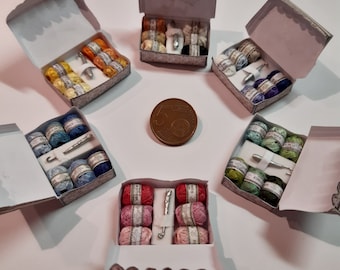 May include: Six miniature boxes filled with colorful yarn balls and knitting needles. The boxes are open and arranged in a circle on a white surface.