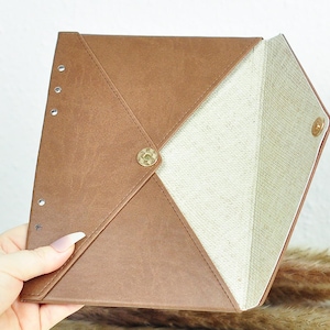 May include: A brown leather envelope clutch with a white fabric lining. The envelope has a flap closure and a gold metal button.