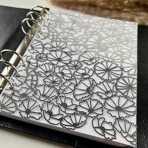 Może przedstawiać: Czarny segregator ze srebrnymi kółkami i przezroczystym wkładką z srebrnym wzorem kwiatowym.