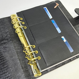 May include: Black leather planner with gold rings and a zippered pocket. The planner has multiple card slots on the inside.