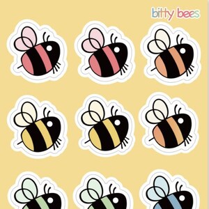 May include: A sheet of stickers featuring cartoon bees in various colors, including pink, orange, yellow, green, blue, and purple. Each bee has a black body with stripes and white accents, and the text "bitty bees" is in the top right corner.