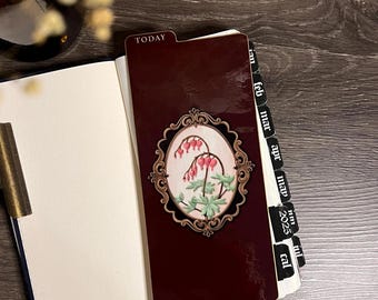May include: A dark maroon planner divider with a tab labeled TODAY and a central oval frame containing a botanical illustration of pink bleeding heart flowers with green leaves. The divider features black monthly tabs for the year 2025.