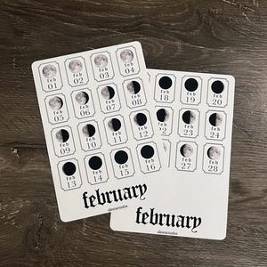 May include: Two white cards with a February moon phase calendar. Each day of the month is represented by a moon phase illustration. The word "february" is written in a decorative font at the bottom of each card.