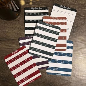 May include: A collection of rectangular sticker sheets labeled Tiny Tabs and Tiny Tabs Type, featuring rows of months from January to December, along with labels for daily, monthly, notes, and calendar. The sheets come in various colors including black, blue, red, and purple with white text.