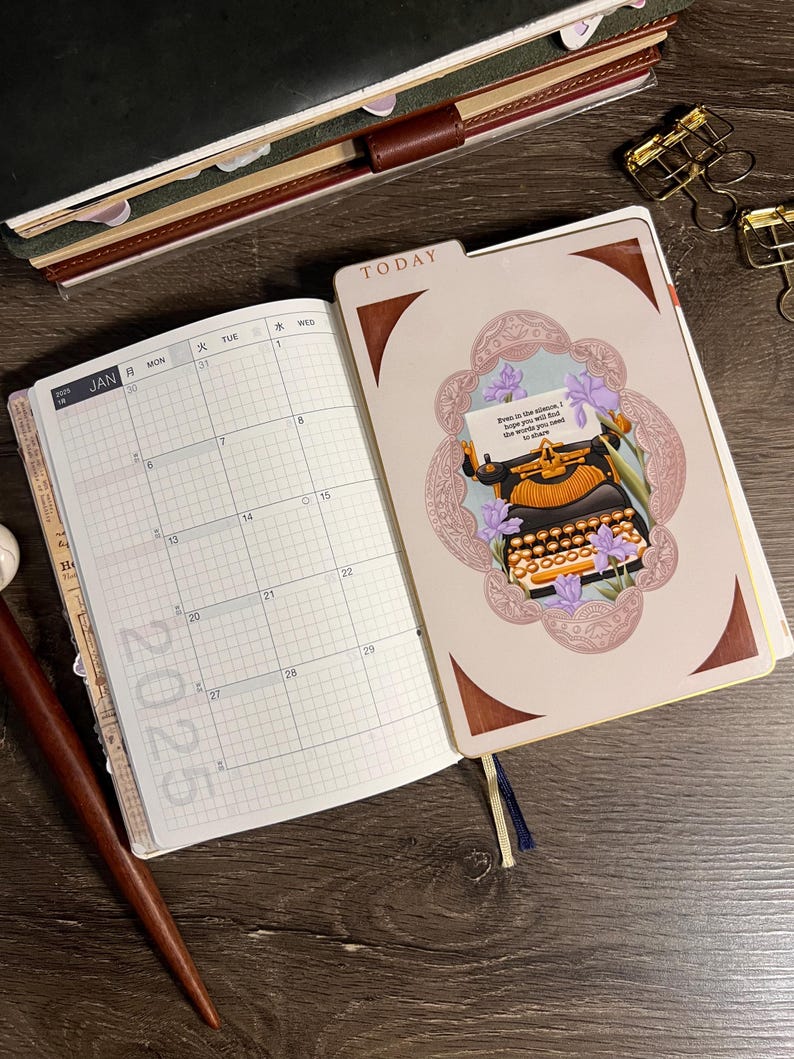 May include: Open planner with a 2025 calendar view and a decorative page featuring a vintage typewriter illustration. The cover reads "TODAY" and the pages are open on a dark wooden surface.