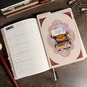 May include: Open notebook with a 2025 calendar and a decorative page featuring a vintage typewriter illustration. The cover reads "TODAY" and has a brown and gold color scheme. Gold binder clips are visible.