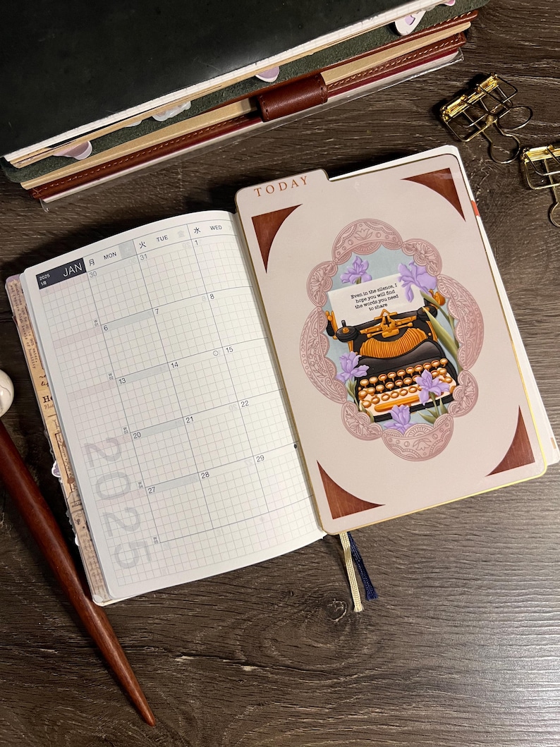 K&ouml;nnte beinhalten: Offenes Notizbuch mit einem Kalender f&uuml;r 2025 und einer dekorativen Seite mit einer Illustration einer alten Schreibmaschine. Der Einband tr&auml;gt die Aufschrift "TODAY" und hat ein braunes und goldenes Farbschema. Goldene B&uuml;roklammern sind sichtbar.