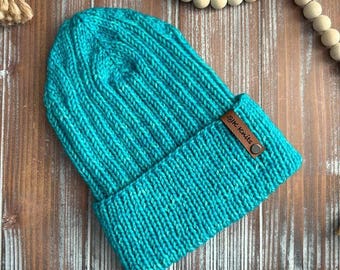 May include: A teal blue knitted beanie with a brown leather label that says "SJK knits".