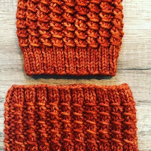 May include: A set of two knitted hats in a burnt orange color. The hats are made with a textured stitch pattern.