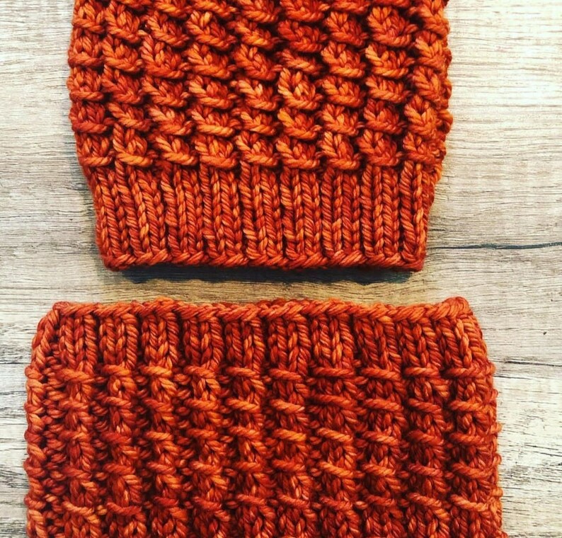 May include: A set of two knitted hats in a burnt orange color. The hats are made with a textured stitch pattern.
