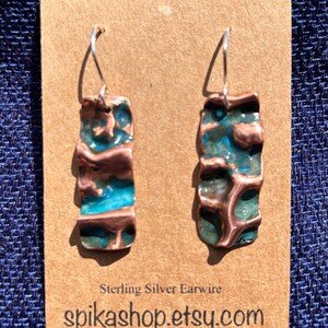 May include: A pair of earrings with a turquoise and copper design. The earrings are made of copper and have a textured surface. The earrings are attached to sterling silver ear wires. The earrings are displayed on a brown card with the text "Sterling Silver Earwire" and "spikashop.etsy.com".
