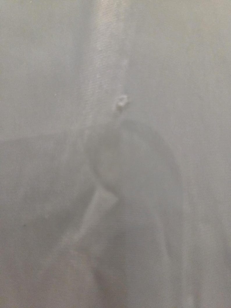 May include: A close-up of a light gray fabric with a small tear. The fabric appears to be smooth and possibly a lightweight material. The tear is located near the center of the image.