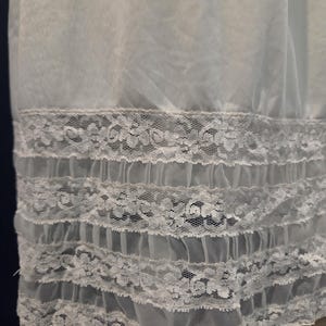 May include: A light blue slip with a delicate lace trim. The lace is white and features a floral pattern. The slip has multiple layers of ruffles at the hem, creating a soft, flowing look. The fabric appears sheer and lightweight.