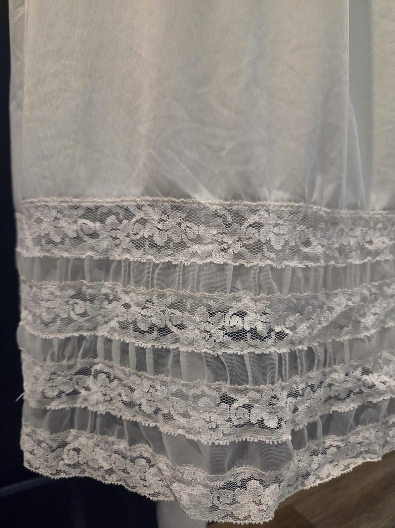 May include: A light blue slip with a delicate lace trim. The lace is white and features a floral pattern. The slip has multiple layers of ruffles at the hem, creating a soft, flowing look. The fabric appears sheer and lightweight.