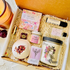 May include: A gift box filled with self-care items, including a bath and body soap, a lip balm, a bath bomb, a candle, and a small bottle of essential oil. The box is decorated with a brown and white shredded paper. The items are all labeled with the text "My Daily Mantra".